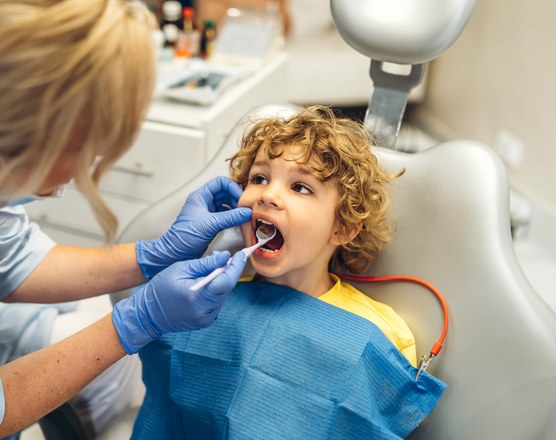 A dentist in gloves examining the inside of a young boy's mouth