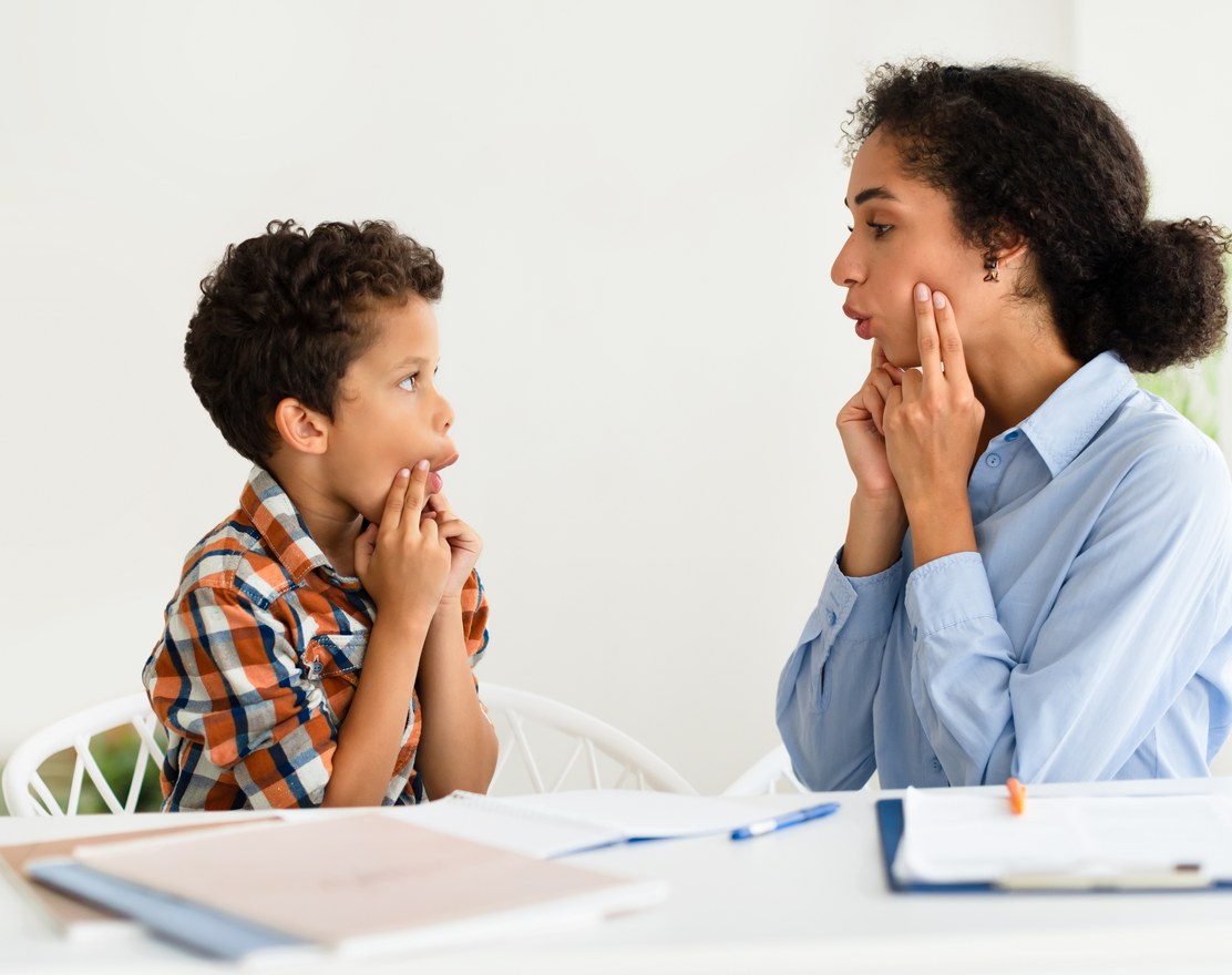 A speech therapist and a boy practicing a sound together