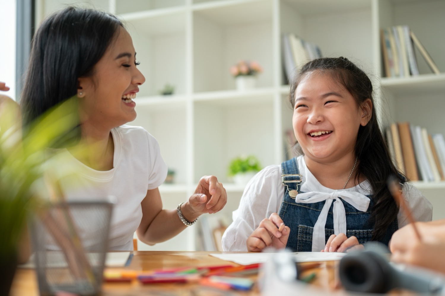 An adult and a child laughing together while drawing at a table