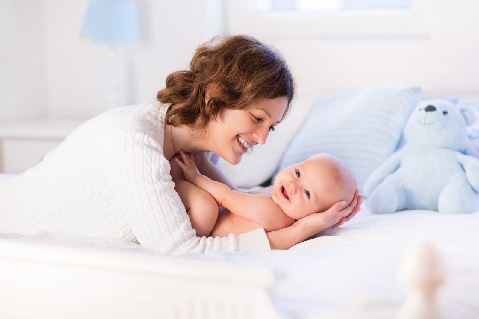 A mother leaning over her smiling newborn on a bed