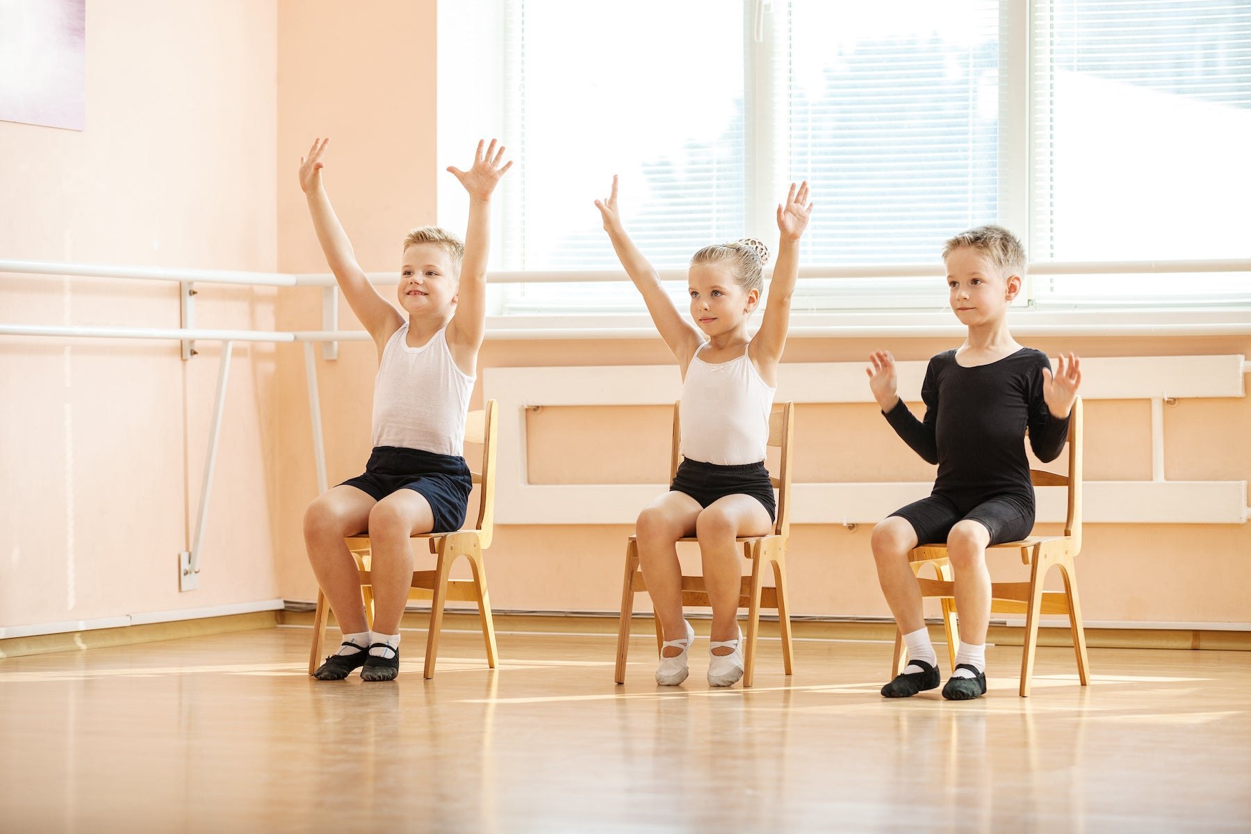 Three children doing a seated stretch with their arms above their heads, still on their chairs