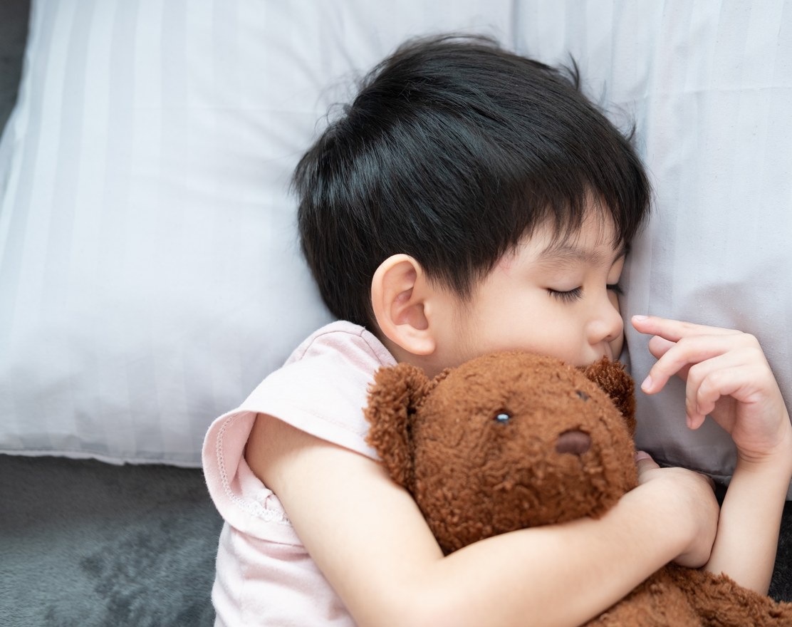 A young child asleep on a pillow, holding a teddy bear