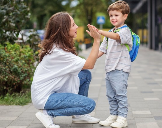 A parent crouching to high-five a young boy wearing a backpack on the way to school