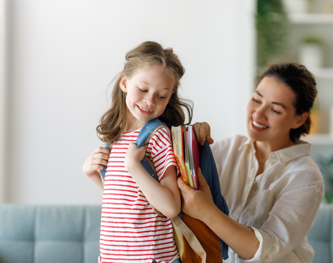 A mother helping her daughter put on a school backpack