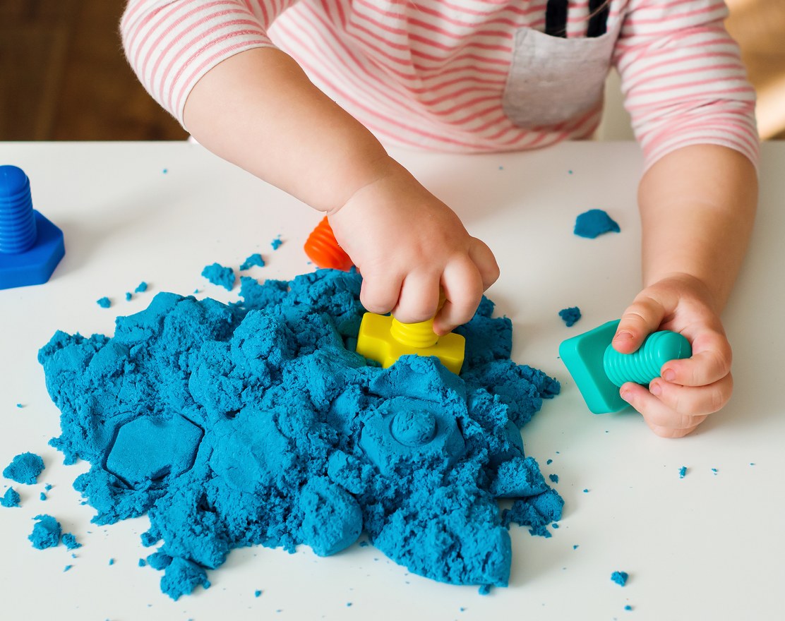 A young child's hands pressing shaped tools into kinetic sand