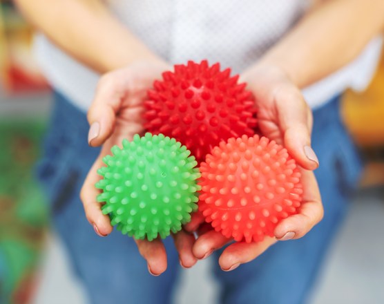 A pair of hands holding three spiky textured sensory balls