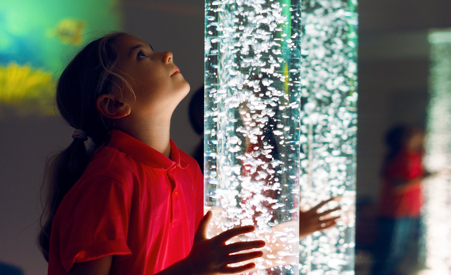 A child at a sensory bubble tube, hands resting on the glass