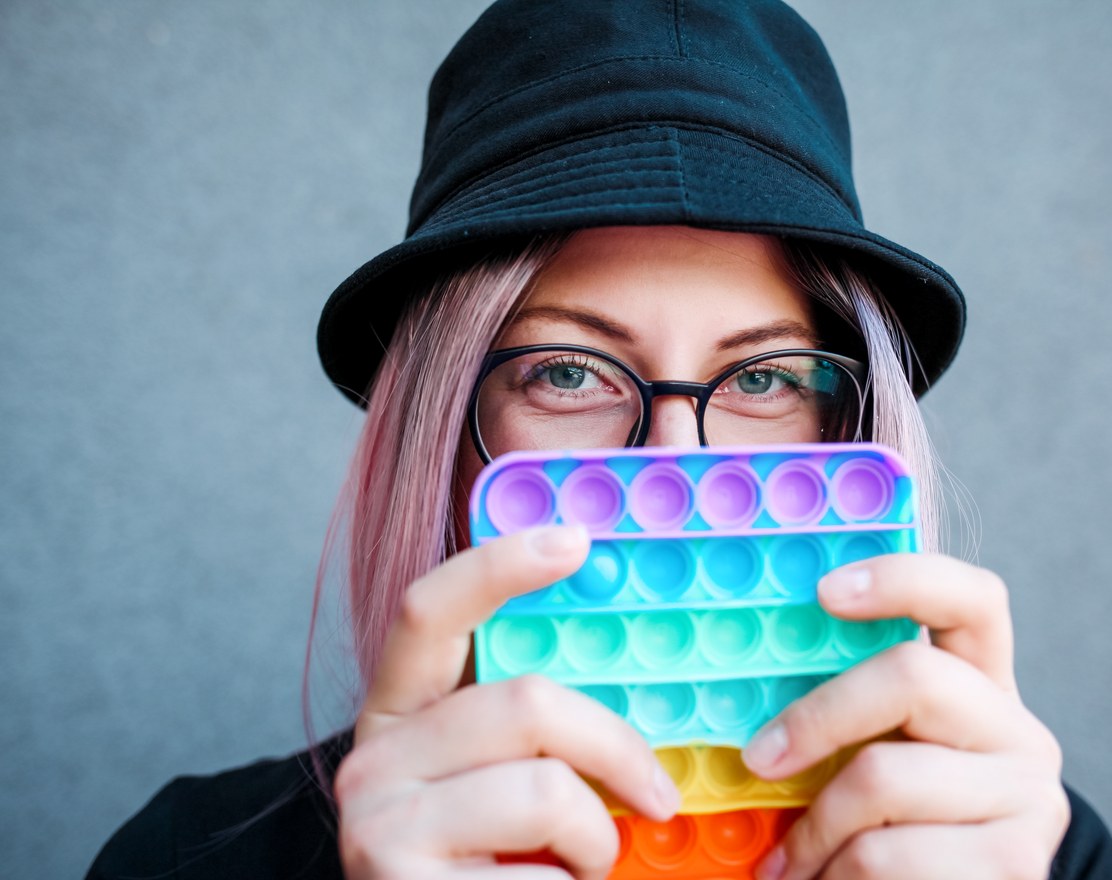 An adult in a bucket hat holding a rainbow pop-it fidget