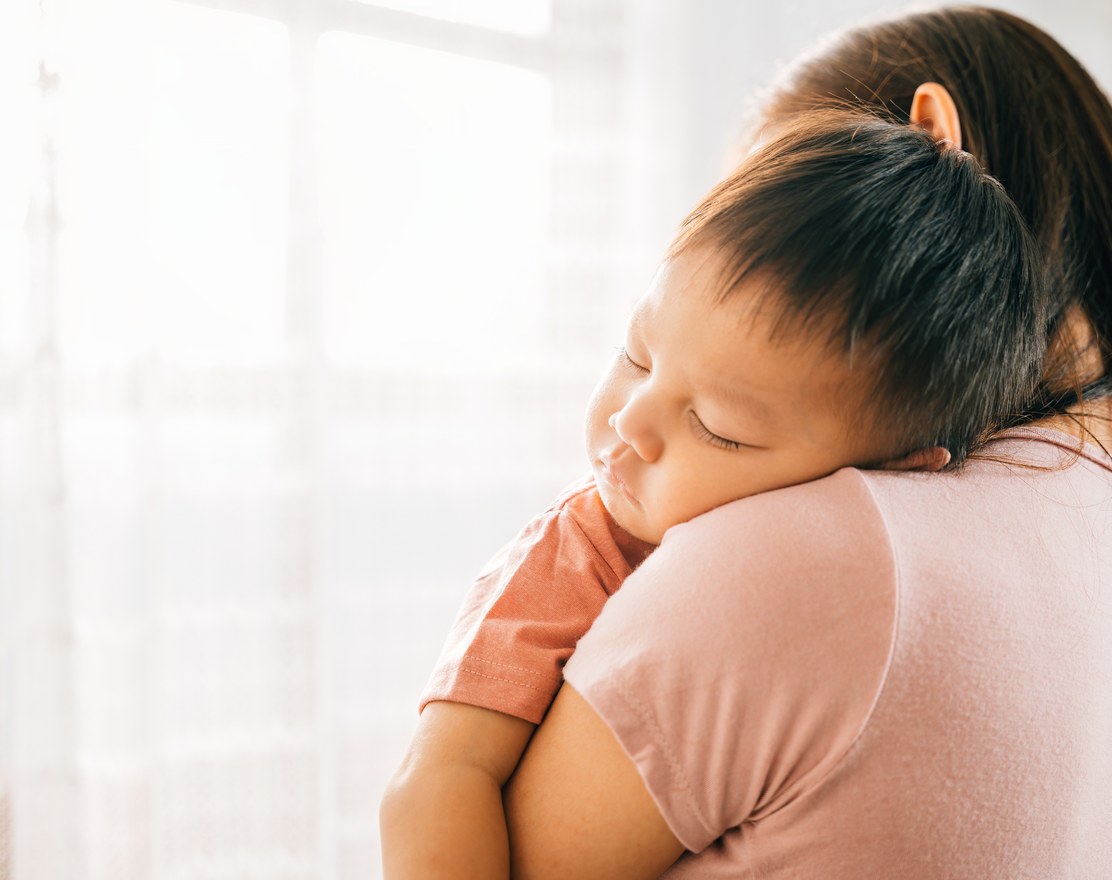 A toddler asleep on a parent's shoulder