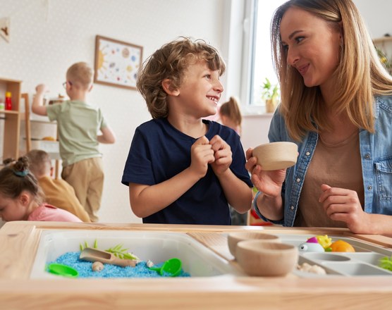 Young children playing at a sensory water table while adults watch
