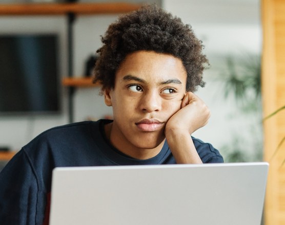 A teenager sitting back from a laptop, looking away from the screen