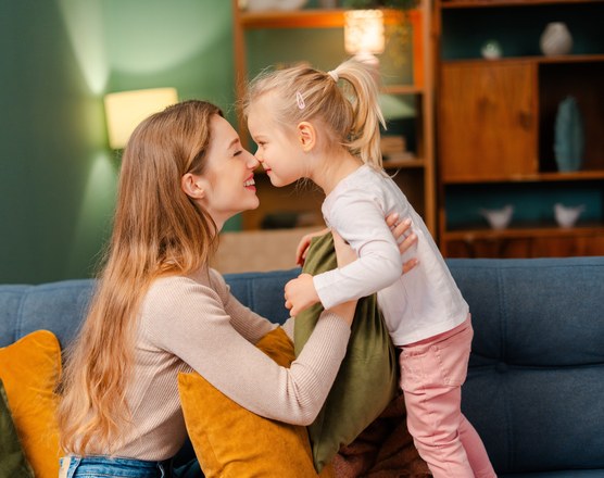 A mother and her young daughter face to face on a sofa, talking closely