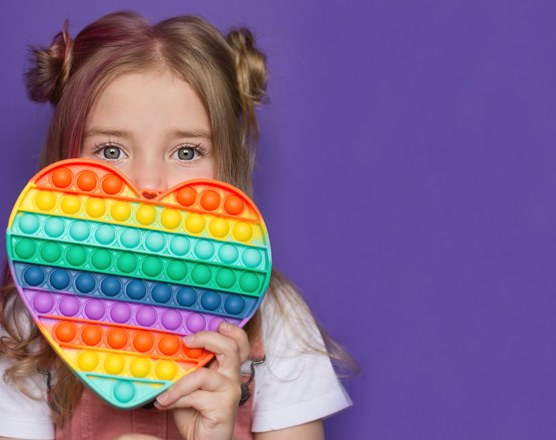 A girl holding a rainbow heart-shaped pop-it fidget up to her face