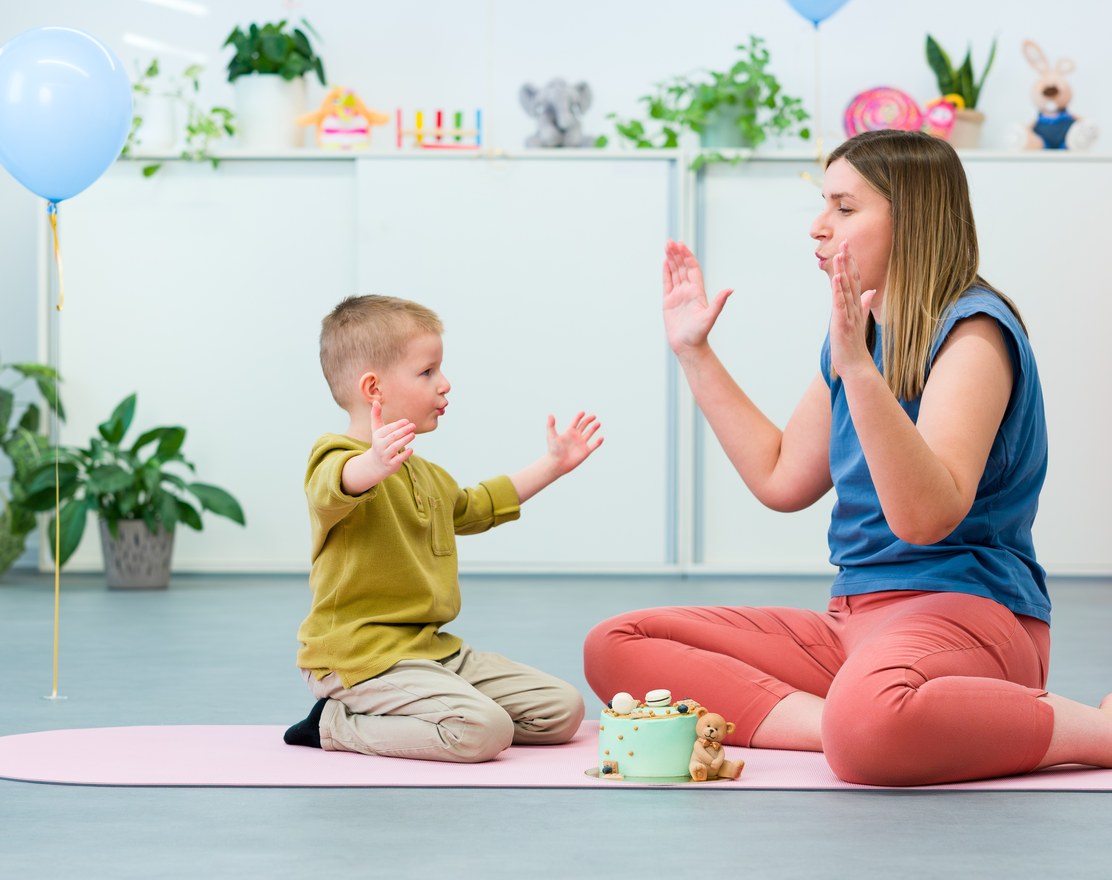 A speech therapist and a young child clapping a rhythm together