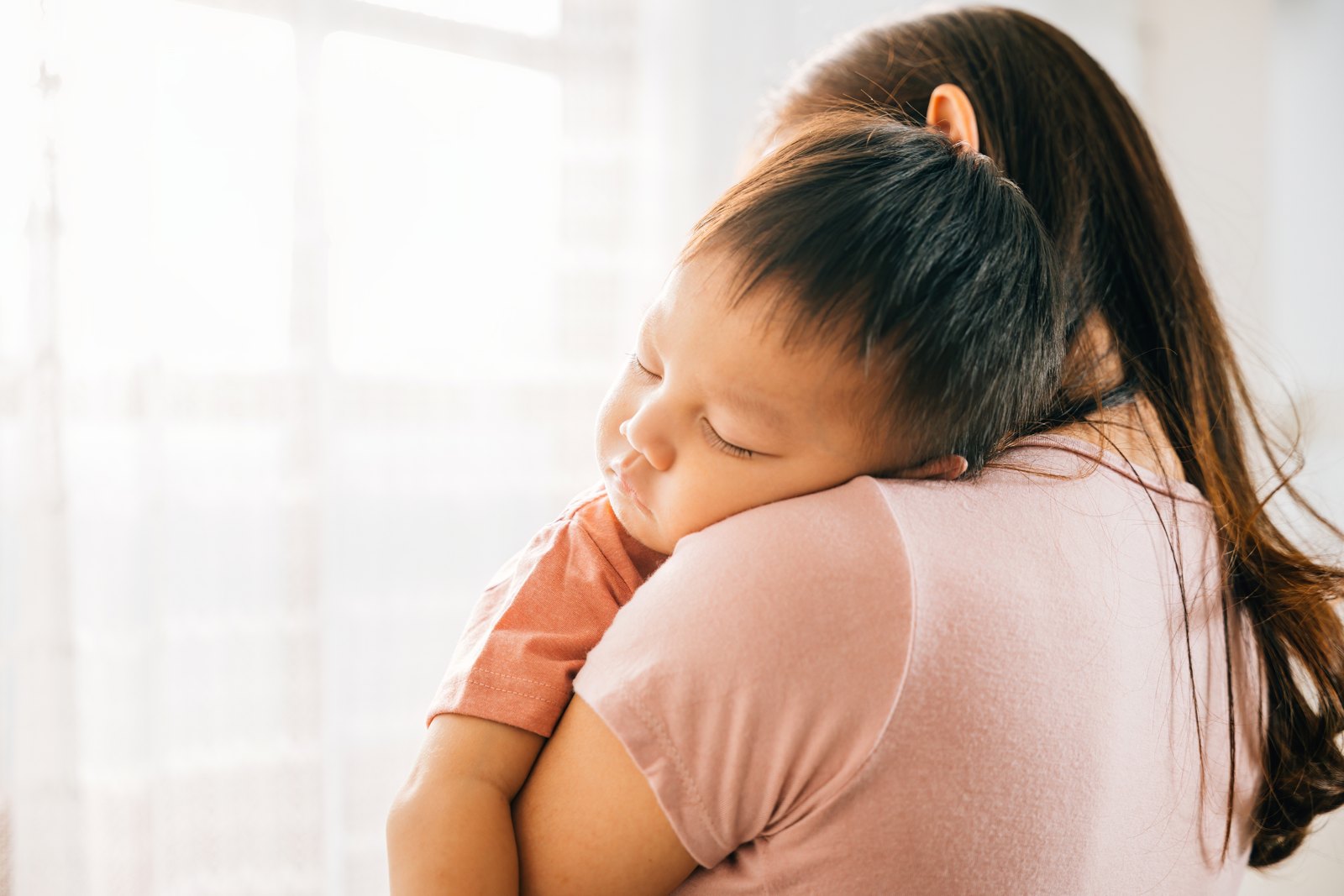 A toddler asleep on their mother's shoulder