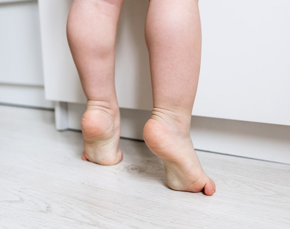 A young child standing on tiptoes on a wooden floor