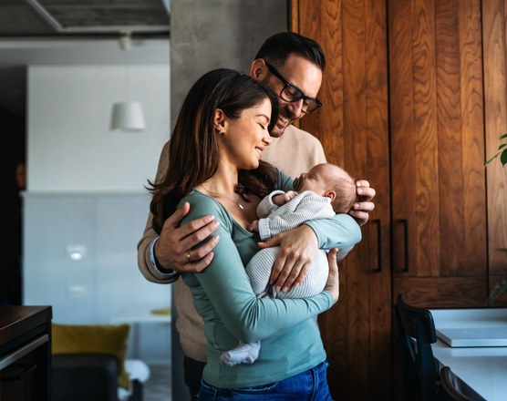 Two parents standing together at home holding their newborn