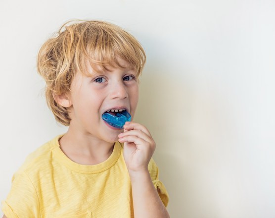 A boy placing a blue mouthguard between his teeth
