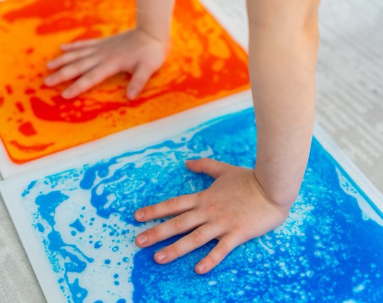 A child's hands pressing into a liquid-filled sensory floor tile