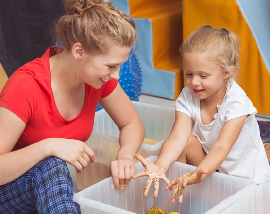 A mother and toddler running their hands through a bin of dried pasta
