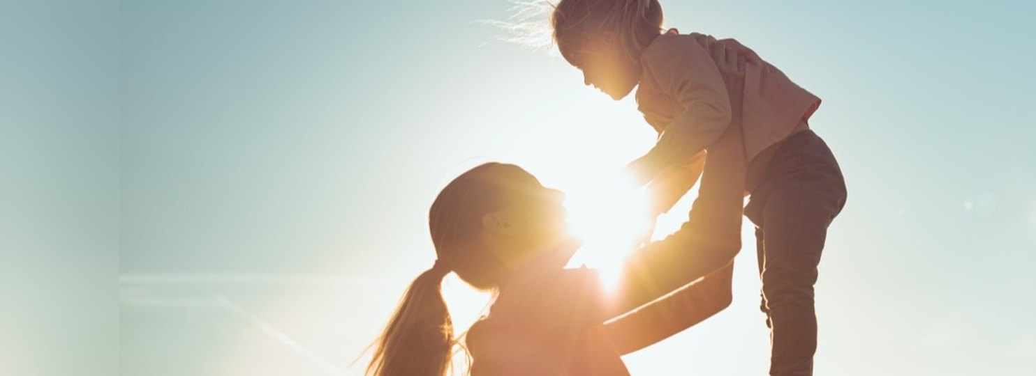 A parent lifting a laughing child into the air in a field at sunset
