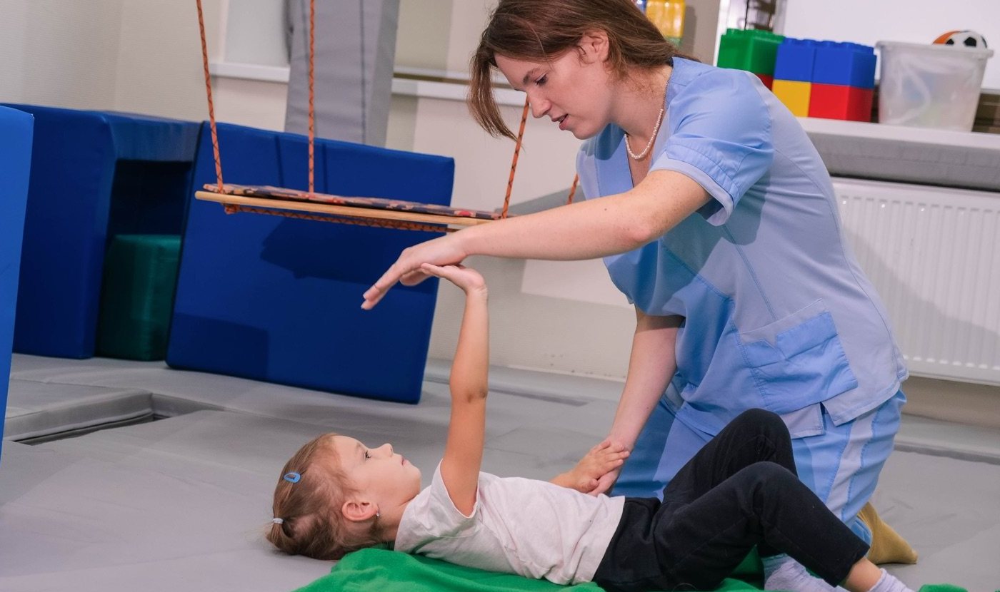 A pediatric therapist guiding a child through a movement exercise on a mat in a sensory gym