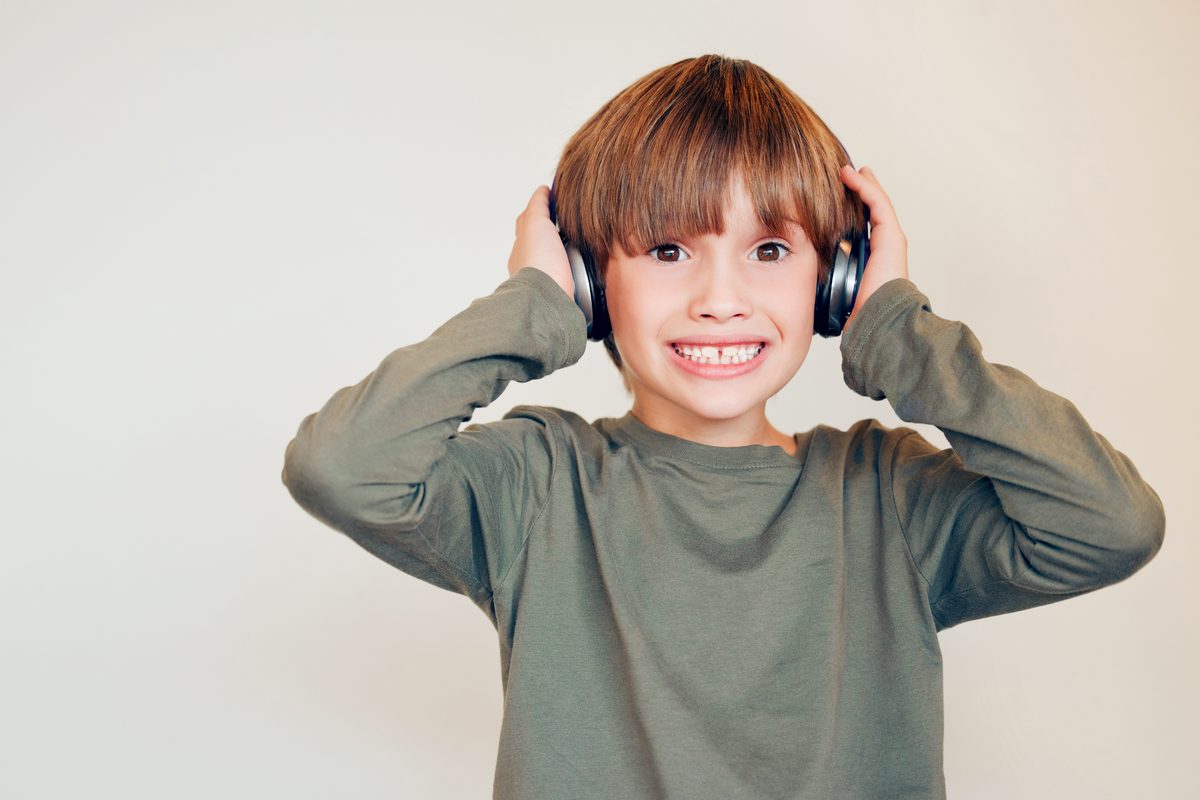 A boy pressing a pair of over-ear headphones to his ears with both hands
