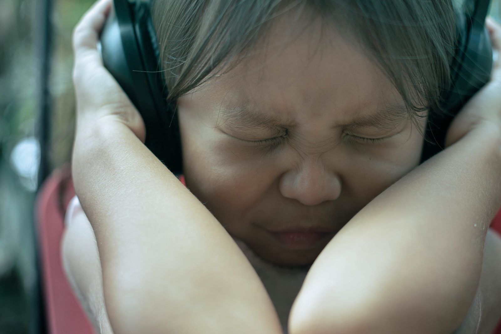 A young child squeezing their eyes shut and pressing large headphones over their ears with both hands