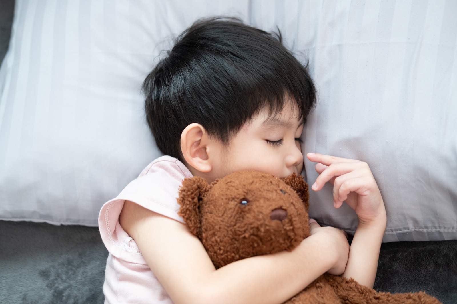 A young child asleep on a pillow, hugging a brown teddy bear