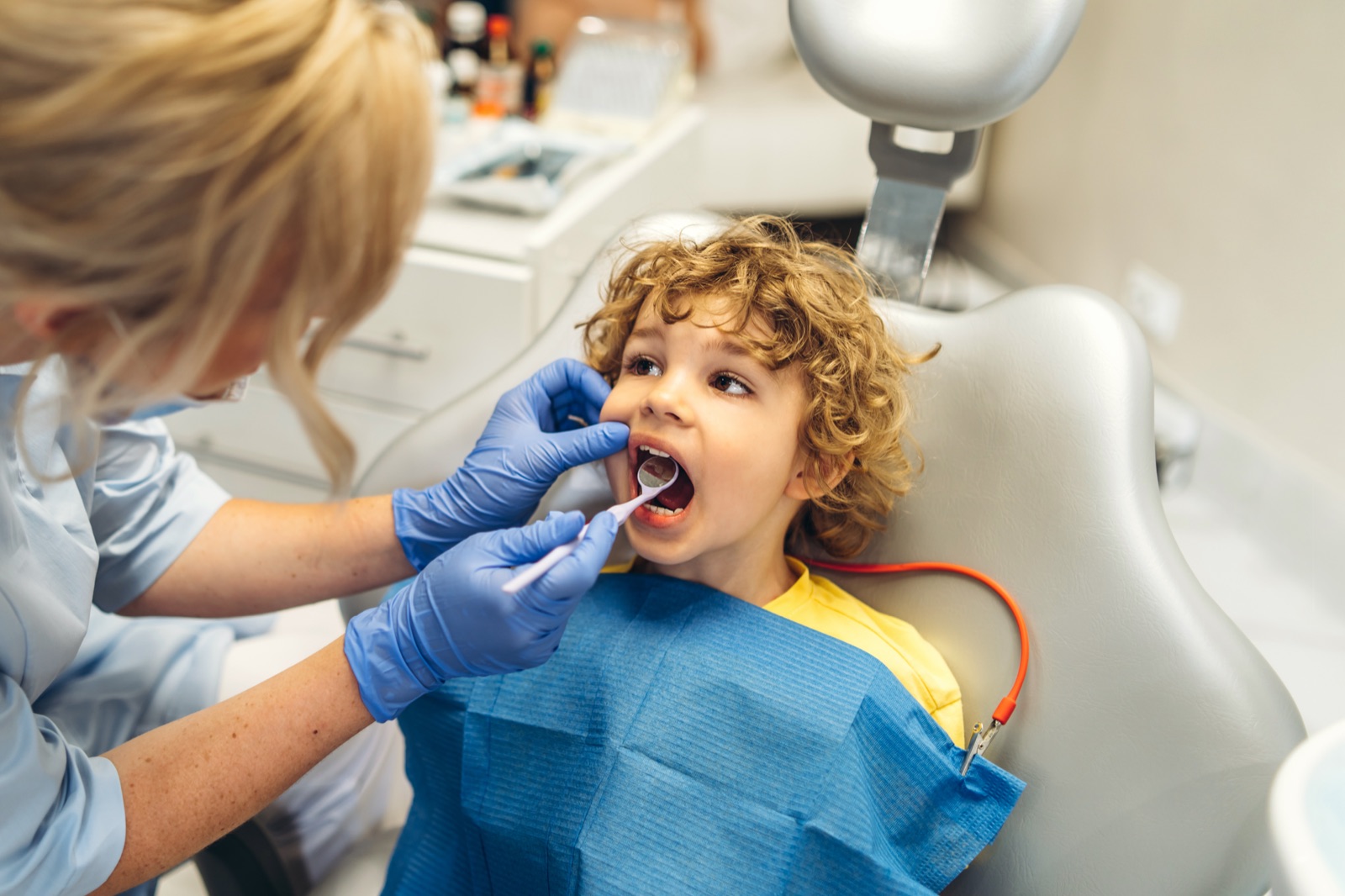 A dentist in blue gloves examining a young boy's teeth with a mirror while he sits calmly in the chair
