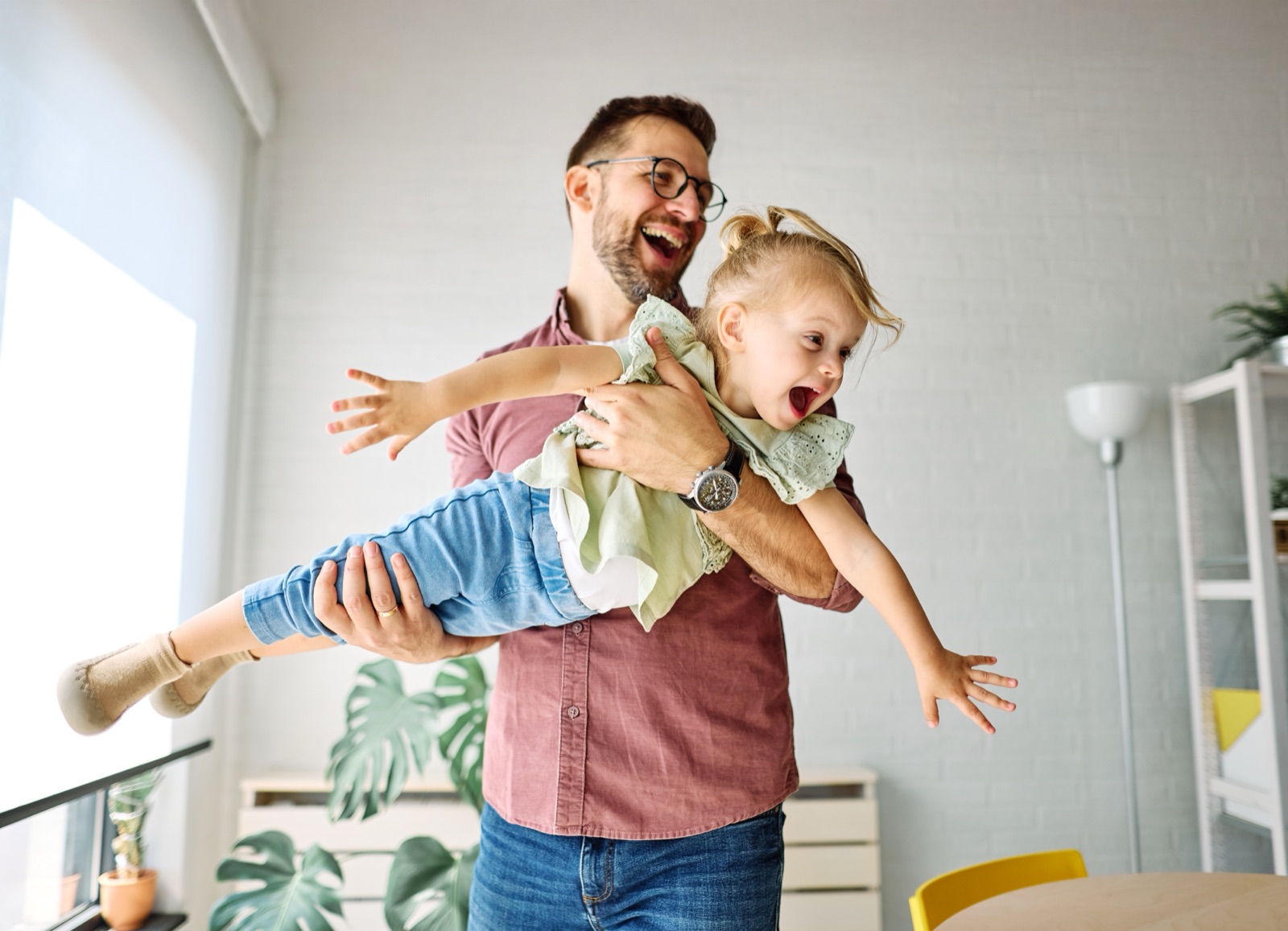 A parent swinging a laughing child through the air in a living room