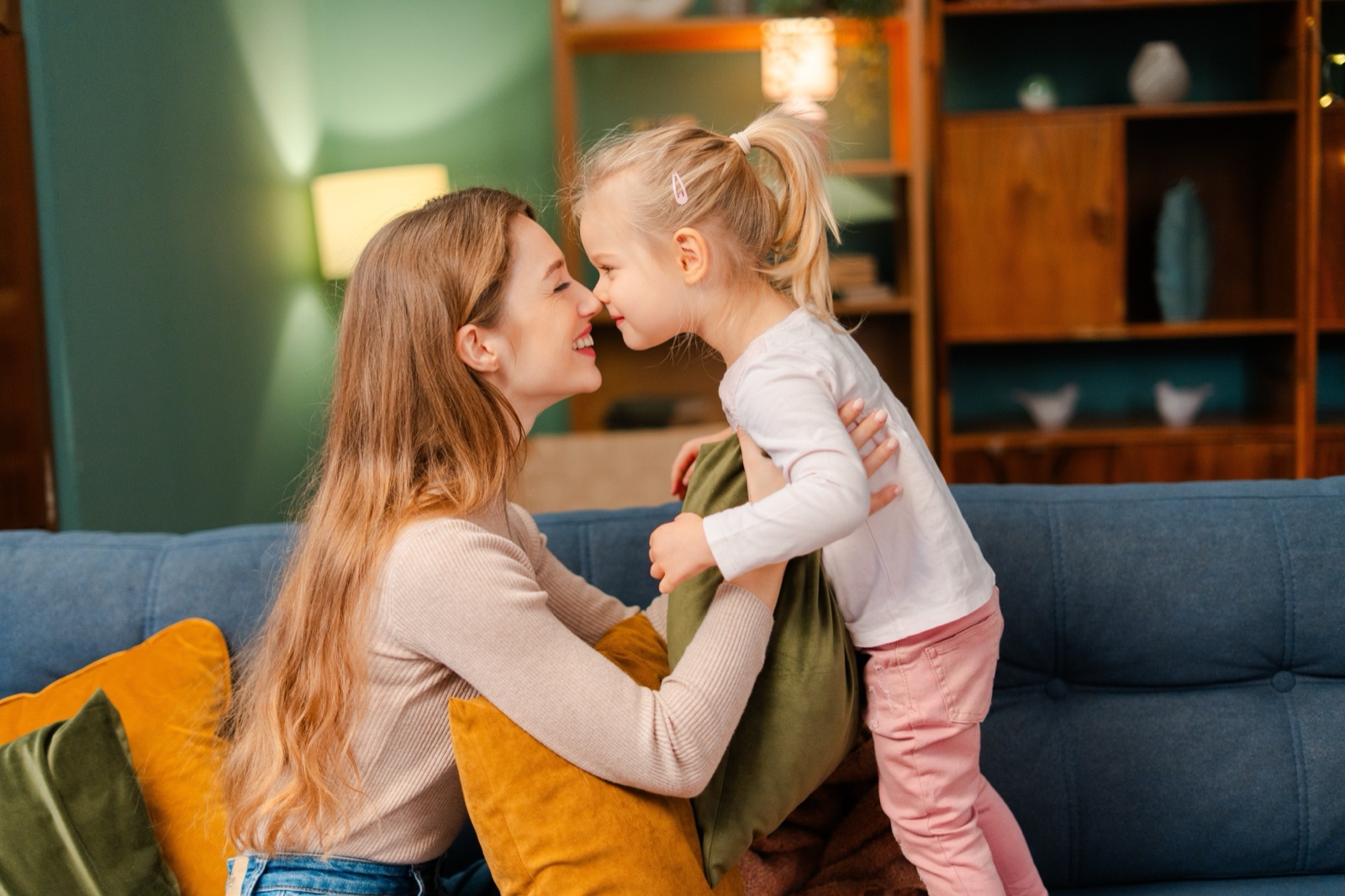 A parent and a young child face to face on a sofa, both smiling