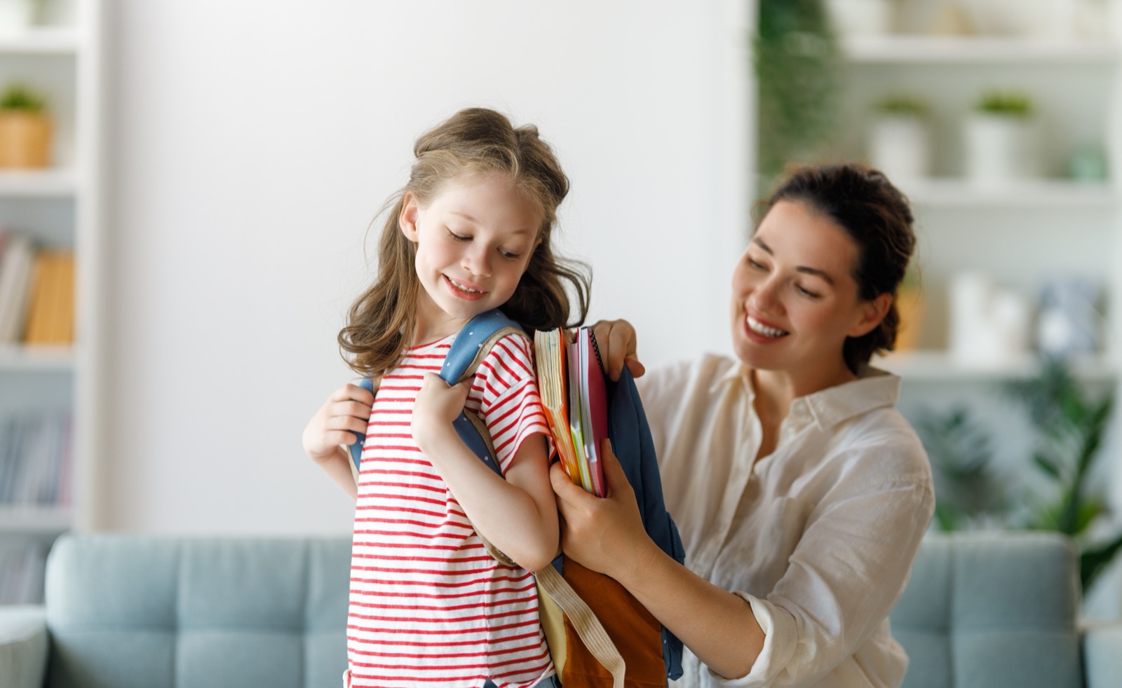 A parent helping a child load books into a school backpack at home